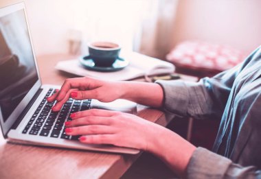 Evinden ahşap masada kitaplarla uzaktan çalışırken dizüstü bilgisayarda yazan isimsiz kadın serbest yazar.