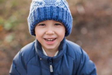 Yukarıdan mavi ceketli ve örgü şapkalı şirin çocuk ilgiyle kameraya bakıyor ve soğuk havada bulanık parka gülümsüyor.