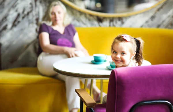 카페의 탁자에 불규칙 여성의 카메라를 미소짓는 어린이 — 스톡 사진