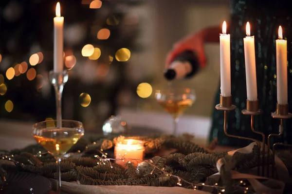 在圣诞晚会上 当她站在宴会桌旁燃着蜡烛时 难以辨认的女性在酒杯中倒入了香槟 — 图库照片