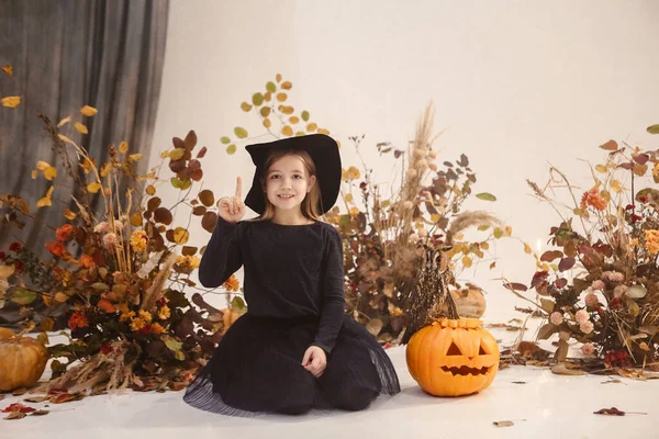 黒のドレスとハロウィンの間に背景に秋の装飾と帽子のシーンに長い髪の立っている小さなかわいい女の子 — ストック写真