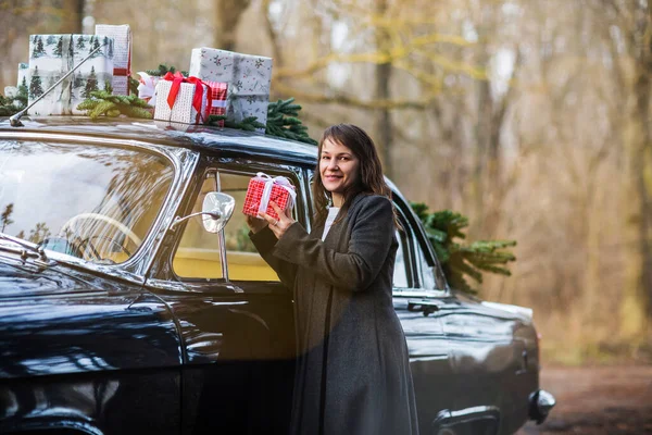 Uśmiechnięta Dorosła Kobieta Ciepłych Ubraniach Przez Zabytkowy Samochód Prezentami Świątecznymi — Zdjęcie stockowe