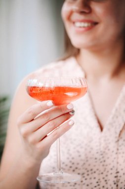 Hafta sonu evde dinlenirken gülümseyen ve pembe alkollü içeceklerin tadını çıkaran çiftçi mutlu kadın.
