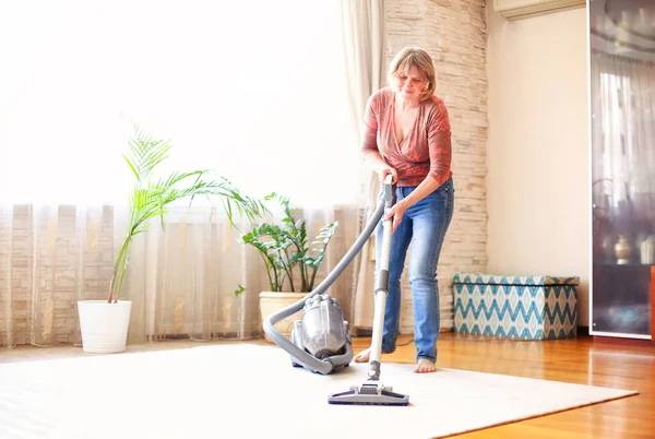 Uśmiechnięta Dojrzała Kobieta Pomocą Odkurzacza Sprzątania Dywanu Podłodze Przytulnym Mieszkaniu — Zdjęcie stockowe