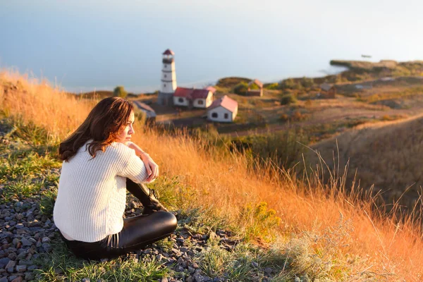 秋の日差しを背景に灯台と青い海の近くに若い女性 — ストック写真
