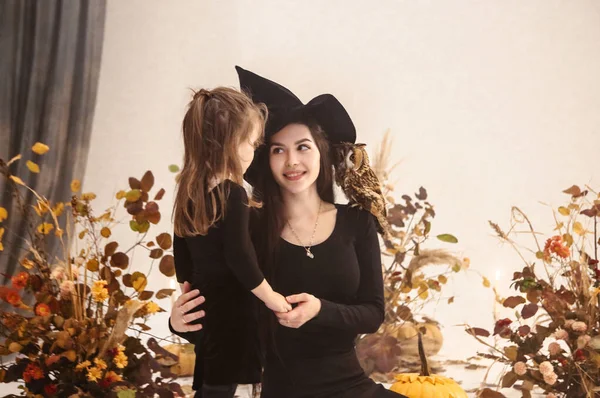 幸せな母親と娘身に着けています不気味な黒衣装の魔女でスタジオでハロウィンの装飾 — ストック写真
