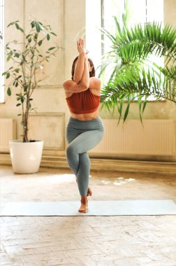 Evde geniş bir odada yoga yaparken mindere oturmuş bakışlarını çeviren zinde bir kadın.