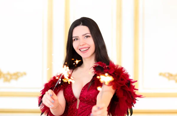 Uśmiechnięta Brunetka Luksusowej Czerwonej Sukni Trzymająca Błyszczące Ognie Stojąc Świetlicy — Zdjęcie stockowe