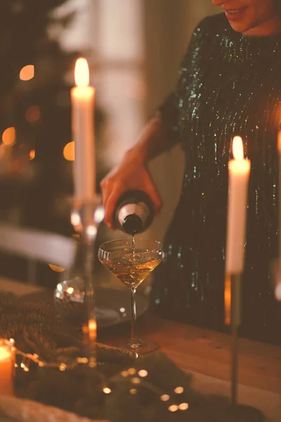 家庭でクリスマスパーティー中にろうそくと宴会テーブルの近くに立っている間にシャンパンと認識できない女性の充填ワイングラス — ストック写真