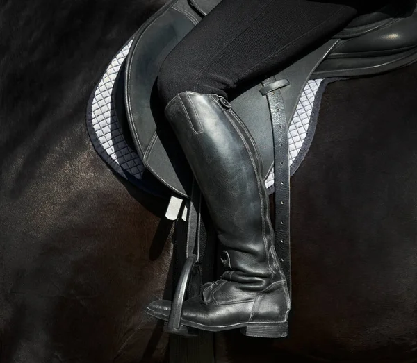 骑在黑马上的骑手的脚靠得很近 站在由马鞍组成的黑色马鞍上的女人的脚掌 — 图库照片