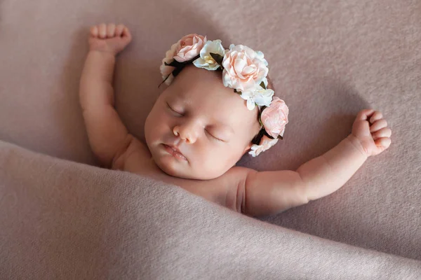 Linda niña recién nacida con diadema de flores que duerme pacíficamente en una posición divertida . — Foto de Stock