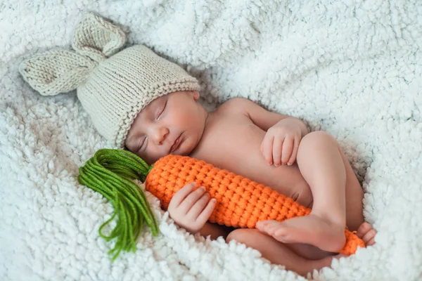 Porträtt av söt sovande nyfödda pojke bär kanin hatt med öron och håller stickad morot. — Stockfoto