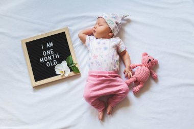 Çiçek bodysuit ve pembe pantolon giyen ve beyaz arka plan üzerinde döşeme bir aylık bebek kız. Havaüstünden vurulmuş.
