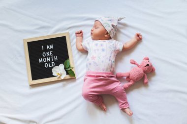 Mektup tahtası ve oyuncak ayı arasında yatan trendy kıyafeti Sevimli bir aylık kız bebek. Bir aylık duyuru.