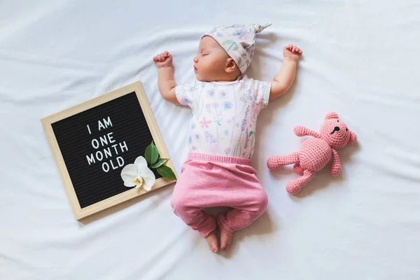 Bir aylık yeni doğmuş kız bebek mektup tahtası ve oyuncak ayı arasında yatıyordu uyku portresi. Düz döşeme kompozisyonu. — Stok fotoğraf