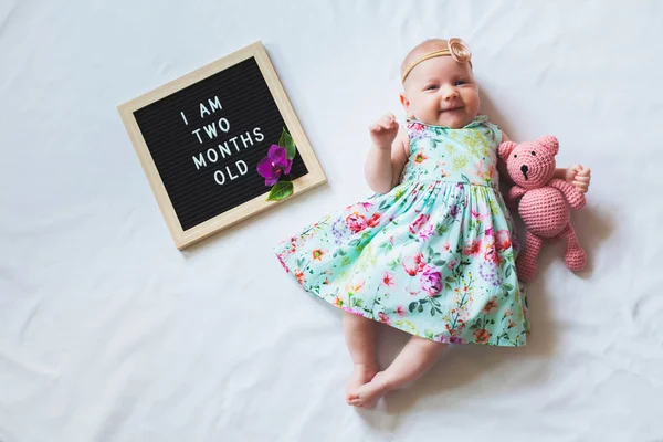 İki aylık kız bebek çiçekli elbise ve kafa bandı beyaz arka plan üzerinde döşeme giyiyor. Havaüstünden vurulmuş.