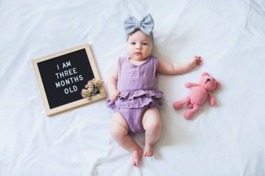 Üç aylık kız bebek mektup tahtası ve oyuncak ayı ile beyaz arka plan üzerinde yatıyordu.