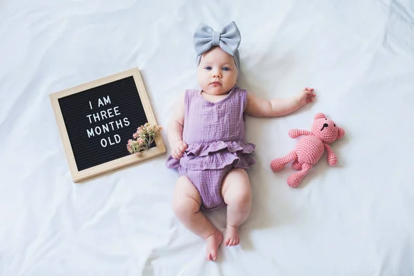 Tre mesi bambina sdraiata su sfondo bianco con cartolina e orsacchiotto . — Foto Stock