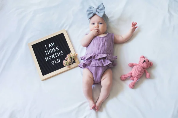 Tiro de sobrecarga de três meses de idade bebê menina que estabelece no fundo branco com placa de carta e ursinho de pelúcia . — Fotografia de Stock