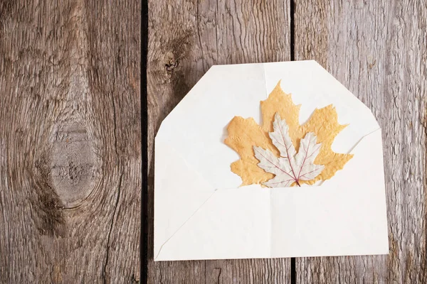 在木质背景的信封上的秋天叶子 — 图库照片