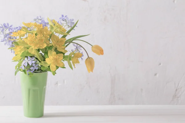 背景古い白壁の上に花瓶で黄色と青の花 — ストック写真
