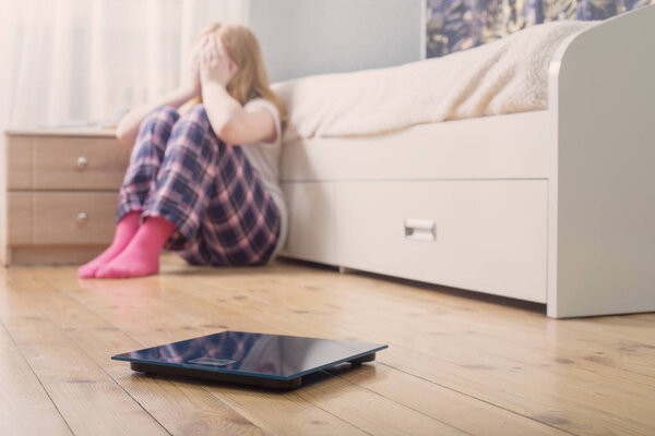 sad teenager girl with scales on floor
