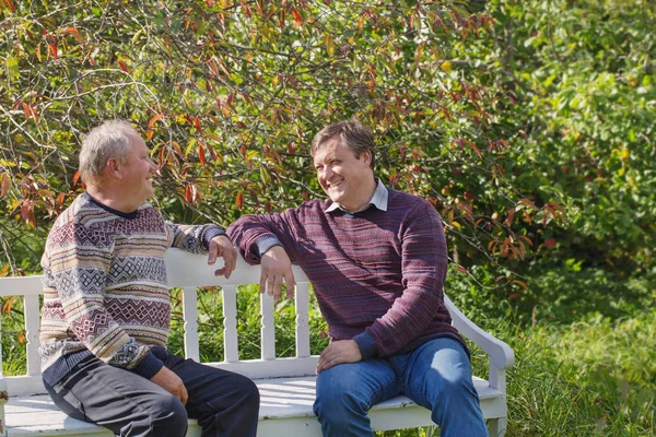 elderly father and son on bench in autumn sunny park