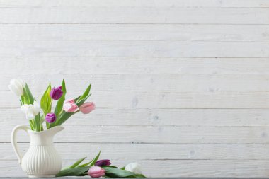 Beyaz ahşap zemin üzerinde beyaz vazoda bahar çiçekleri