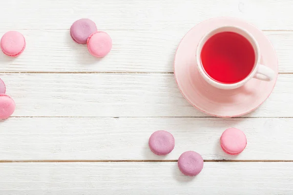 Xícara de chá e macaroons rosa na mesa de madeira branca — Fotografia de Stock