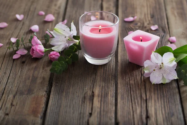 Růžové svíčky a květiny na dřevěné pozadí — Stock fotografie