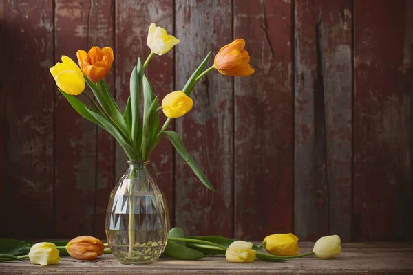 Tulips in glass vase on old wooden background — Stock Photo, Image