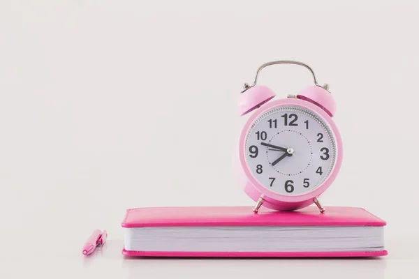 Despertador rosa com notebook sobre fundo branco — Fotografia de Stock