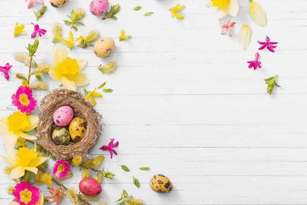 Uova di Pasqua in nido con fiori primaverili su sfondo ligneo — Foto Stock