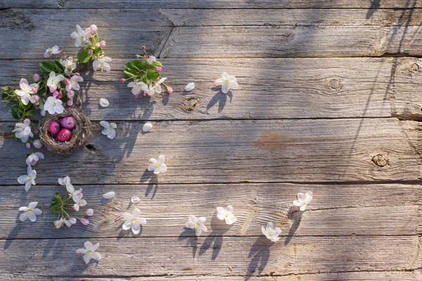 Пасхальные яйца в гнезде с весенними цветами на старом деревянном фоне — стоковое фото