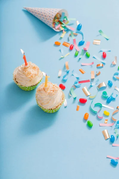 Birthday hat with confetti and cupcake on blue paper background — Stock Photo, Image