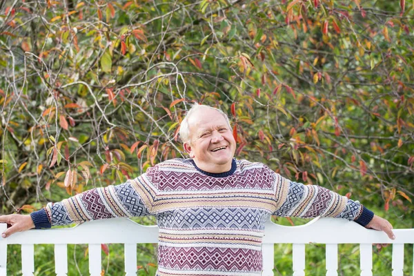 Oudere man rust op witte Bank najaar Park — Stockfoto