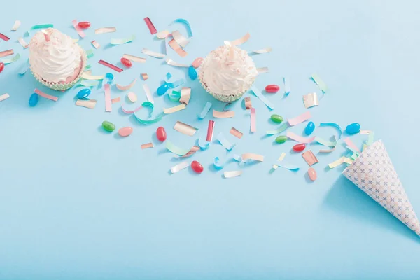 Chapéu de aniversário com confete e cupcake no fundo de papel azul — Fotografia de Stock
