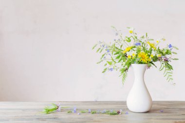 Beyaz vazodaki kır çiçekleri arka plandaki eski duvarda