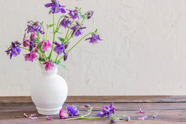 Aquilegia flowers in white vase on wooden table — Stock Photo, Image