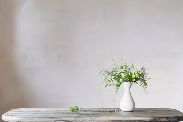 Beyaz vazodaki kır çiçekleri arka plandaki eski duvarda — Stok fotoğraf