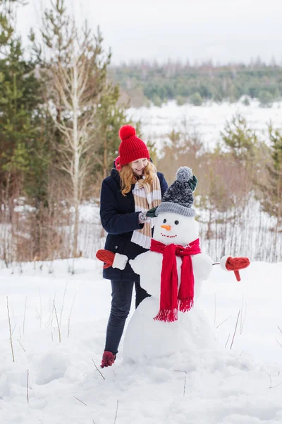 Счастливая девочка-подросток со снеговиком в зимнем лесу — стоковое фото