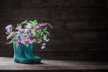 Eski koyu ahşap arka planda kauçuk botlar yaz çiçekleri
