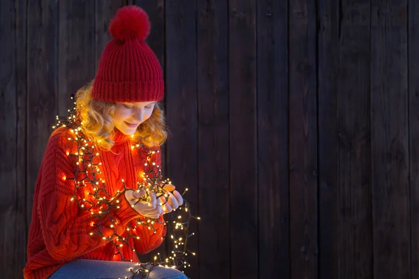 Mädchen mit rotem Hut mit Weihnachtsbeleuchtung auf Holzgrund — Stockfoto