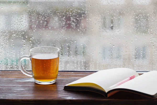 Kopje thee op de achtergrond van het raam met regendruppels bij zonsondergang — Stockfoto