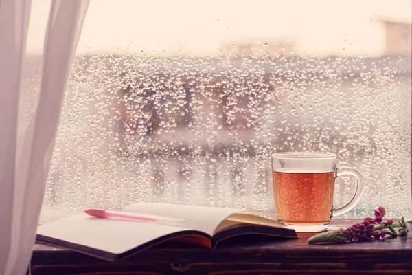 Tasse de thé sur fond de fenêtre avec des gouttes de pluie au coucher du soleil — Photo