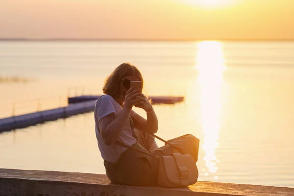 Fille souriante faisant selfie sur fond de coucher de soleil sur la mer — Photo