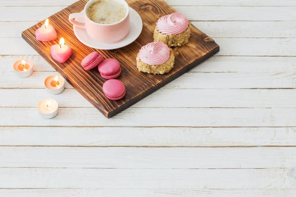 cup of coffee with cakes and burning candles  on white wooden ba