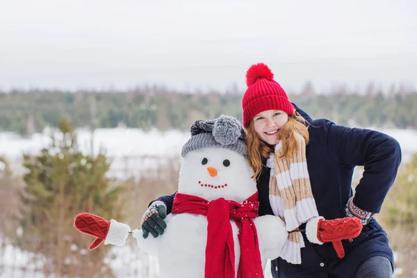 Feliz adolescente chica con muñeco de nieve en invierno bosque — Foto de Stock