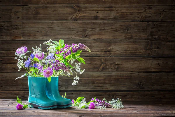 Καλοκαίρι λουλούδια σε καουτσούκ μπότες σε παλιό σκούρο ξύλινο φόντο — Φωτογραφία Αρχείου