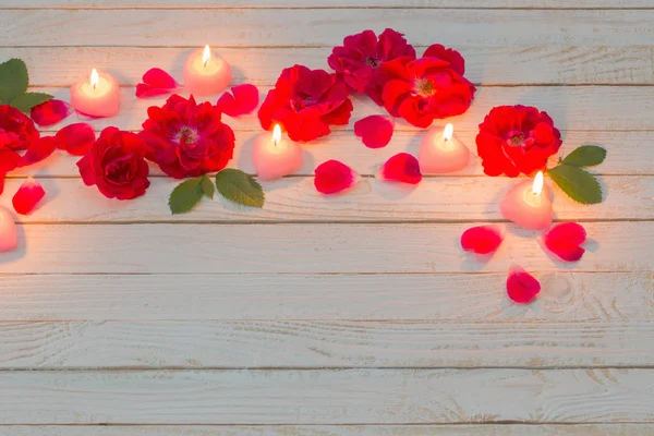 Rose rosse e candele ardenti su sfondo bianco in legno — Foto Stock